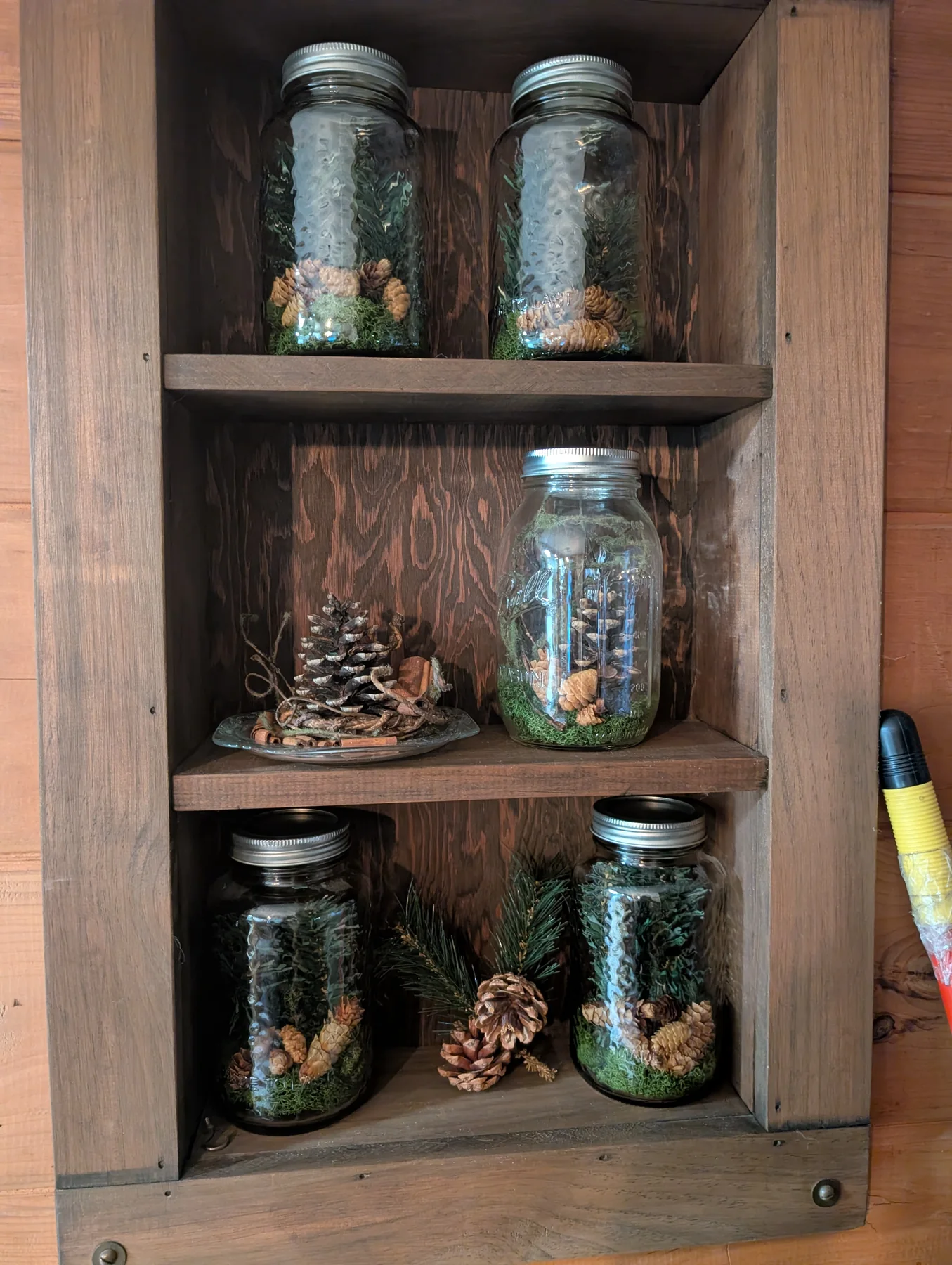 Built-in wood shelf styled with glass jars, pinecones, and evergreen branches